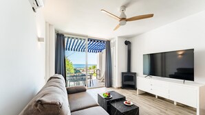 Sala de estar com sofá, televisão, lareira e varanda com vista para o mar.
