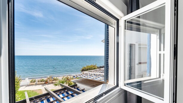 Uma janela com vista para o mar e um espaço de pátio com mobiliário externo.