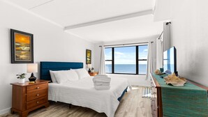 A bedroom with a bed, nightstands, a dresser, a large window with a view of the ocean, and artwork on the walls. - Oceanfront 2BR Condo | Steps to Beach | Sleeps 8 (Ocean City)