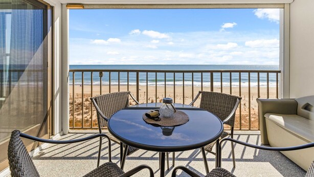 A balcony with a table, chairs, and a view of the beach. - Oceanfront 2BR Condo | Steps to Beach | Sleeps 8 (Ocean City)