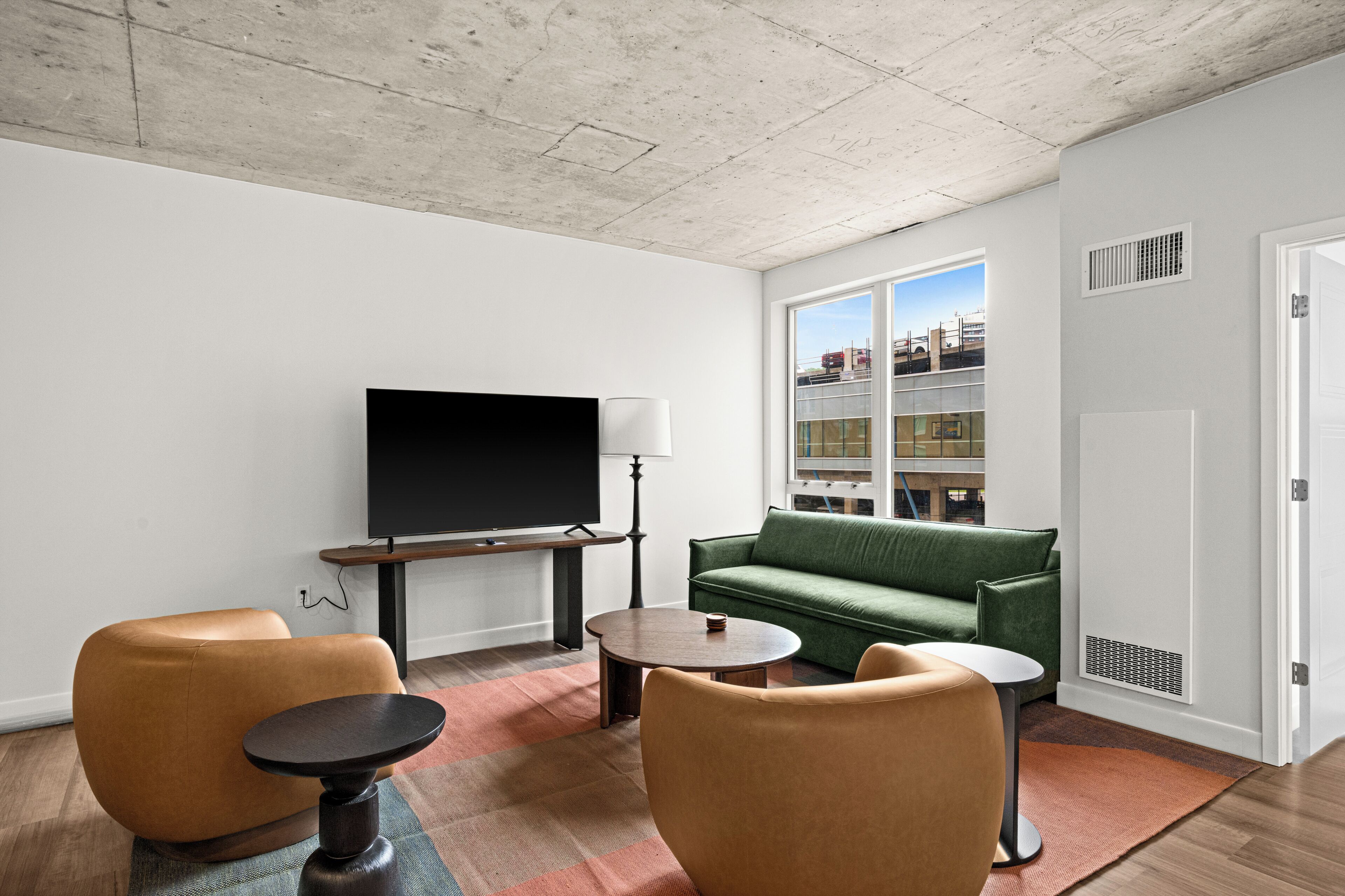 Una sala de estar moderna con televisor de pantalla plana, sofá verde, dos sillones y una mesa de centro.