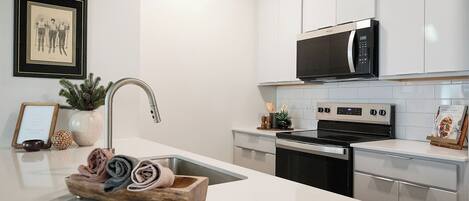 A modern kitchen with stainless steel appliances, a white countertop, and a framed picture on the wall.
