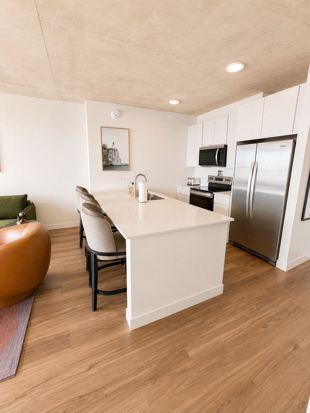 Una cocina moderna con armarios blancos, un refrigerador de acero inoxidable, un microondas y una isla grande con asientos.