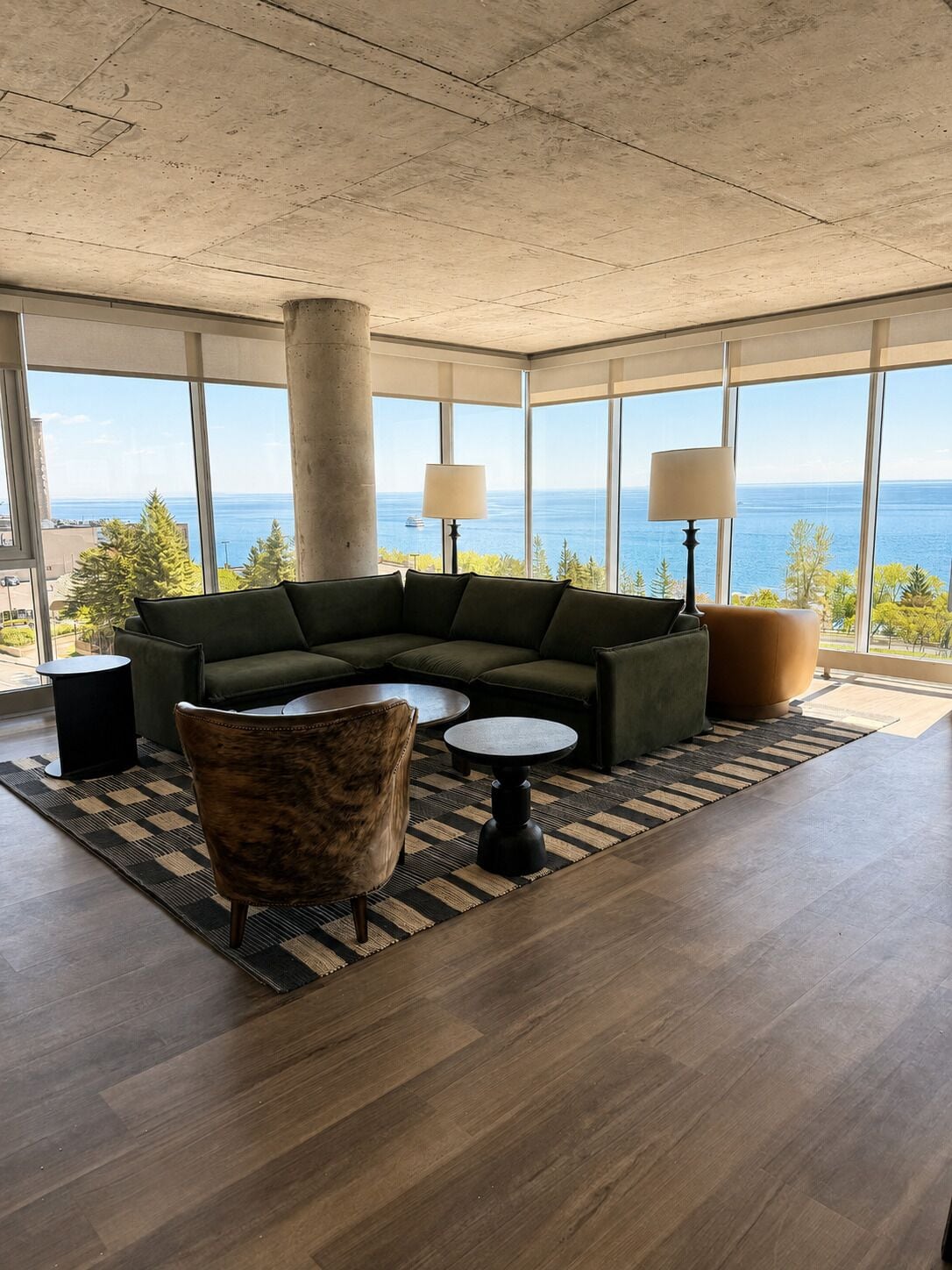 A modern living room with a sectional sofa, two side tables, a patterned rug, and large windows offering a view of the ocean.