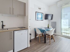 Eine kompakte Küche mit Geschirrspüler, einem Esstisch mit Stühlen, einem gerahmten Bild an der Wand und einem Fernseher, der über dem Tisch befestigt ist.