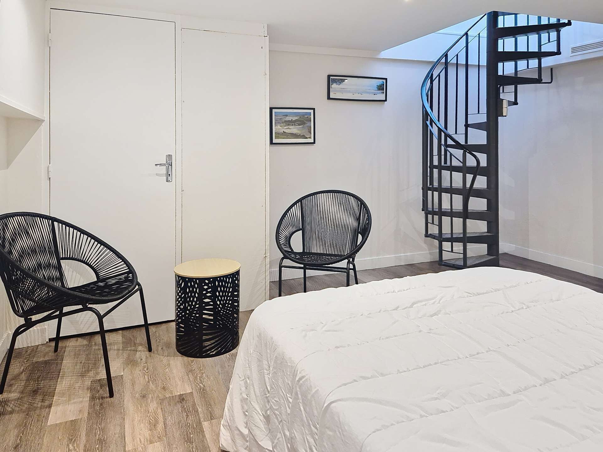 Ein Schlafzimmer mit einem Bett, zwei Stühlen, einem kleinen Tisch, einer Wendeltreppe und zwei gerahmten Bildern an der Wand.