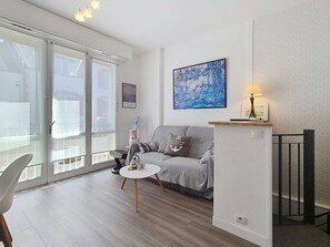 Ein Wohnzimmer mit grauem Sofa, einem kleinen runden Tisch, einer Lampe und einem Gemälde an der Wand.
