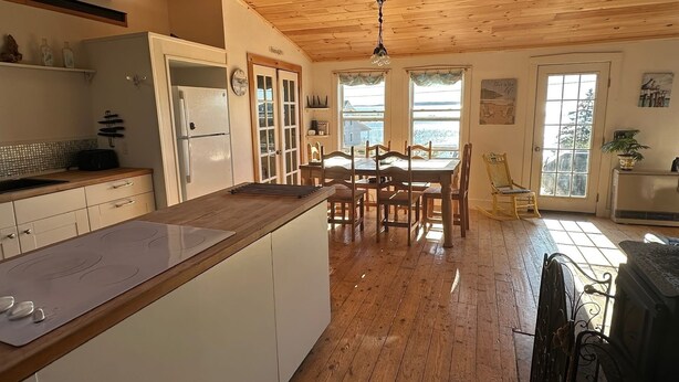 A kitchen with wooden cabinets, a dining table, and chairs, a refrigerator, and a window with curtains.