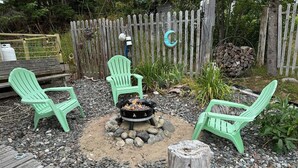 A backyard with a fire pit surrounded by green chairs, a wooden deck, and a rustic fence.