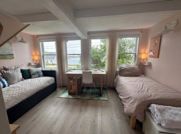A room with two beds, a desk, and a view of the outdoors.