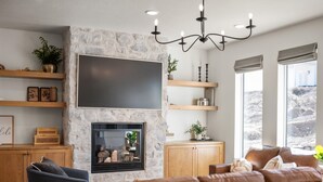 A living room with a stone fireplace, a large flat-screen TV, wooden shelves, a sofa, and a chandelier. - The Hyde Park Mountain Home (Hyde Park)