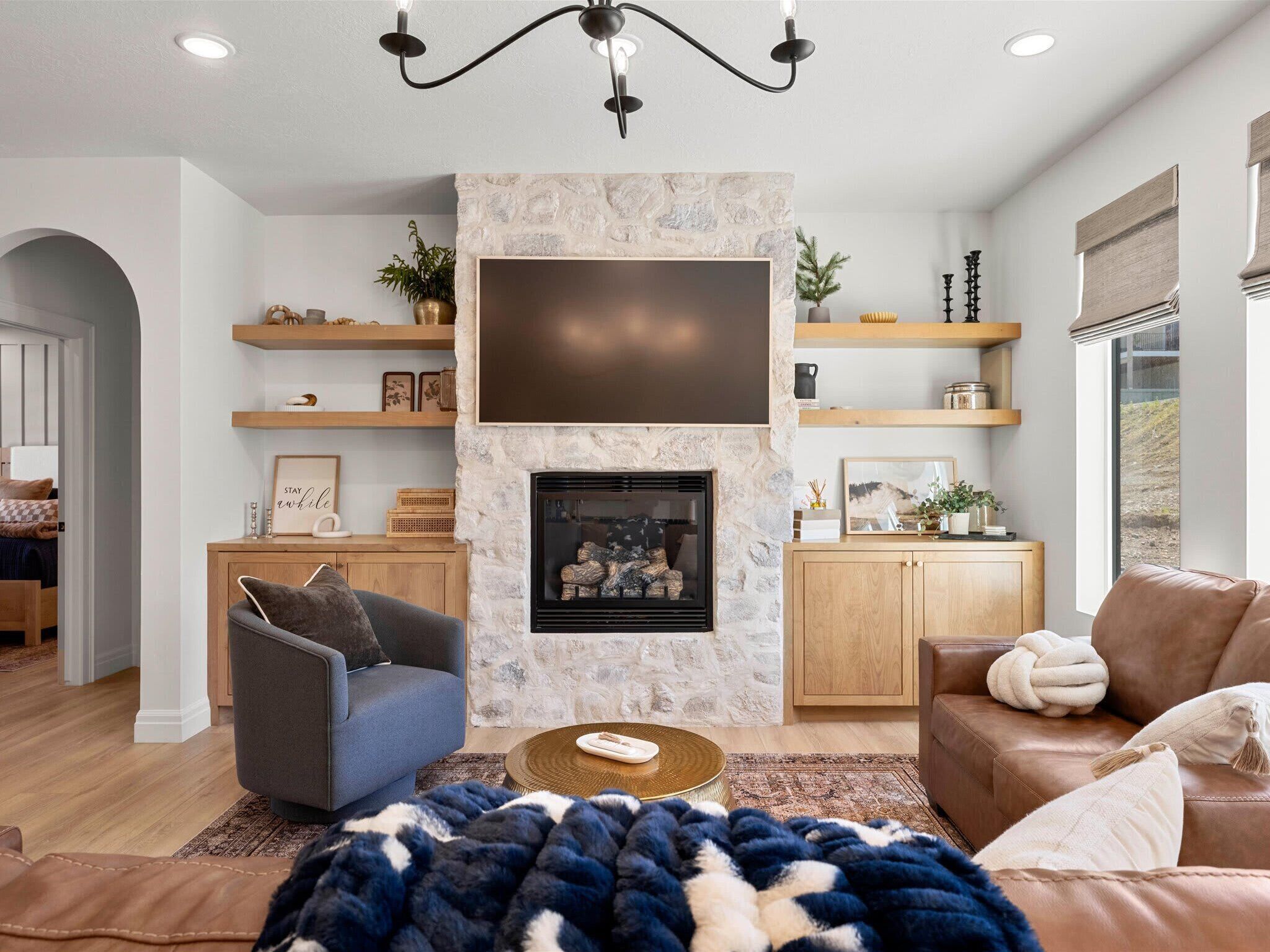 A living room with a stone fireplace, a mounted TV, wooden shelves, and a leather sofa.