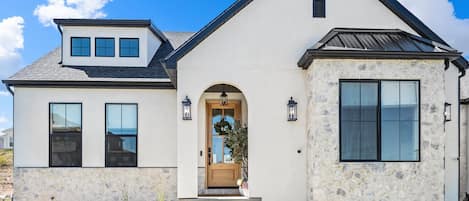 Une maison à deux étages avec une façade en pierre, une entrée à l’avant avec une porte en bois et une grande fenêtre sur le côté droit.