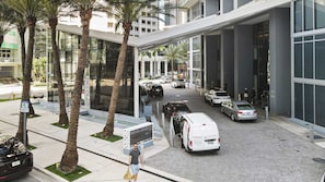 Un edificio moderno con acceso cubierto, palmeras y coches estacionados.