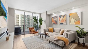 Un salon moderne avec un canapé, un fauteuil et une table basse, de grandes fenêtres et des œuvres d’art abstraites accrochées au mur.