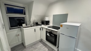 A compact kitchen with white cabinets, a built-in oven, a microwave, and a refrigerator. - Hammersmith Haven (London)