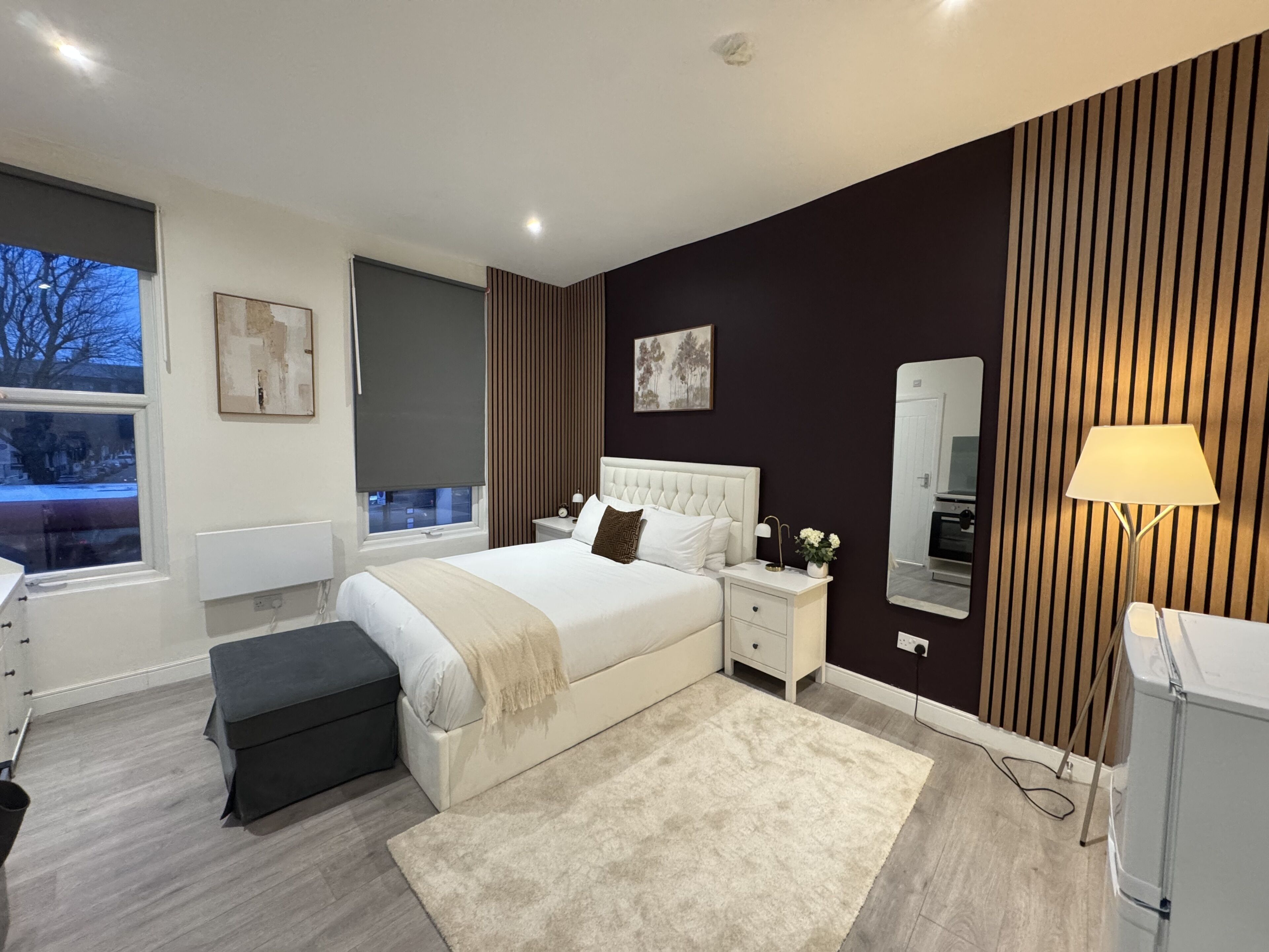 A modern bedroom with a large bed, bedside tables, a mirror, and a window.