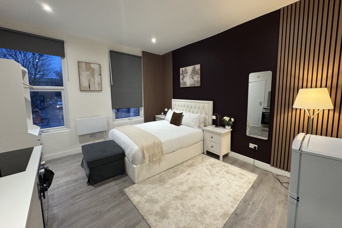 A modern bedroom with a large bed, bedside tables, a mirror, and a view of the street.