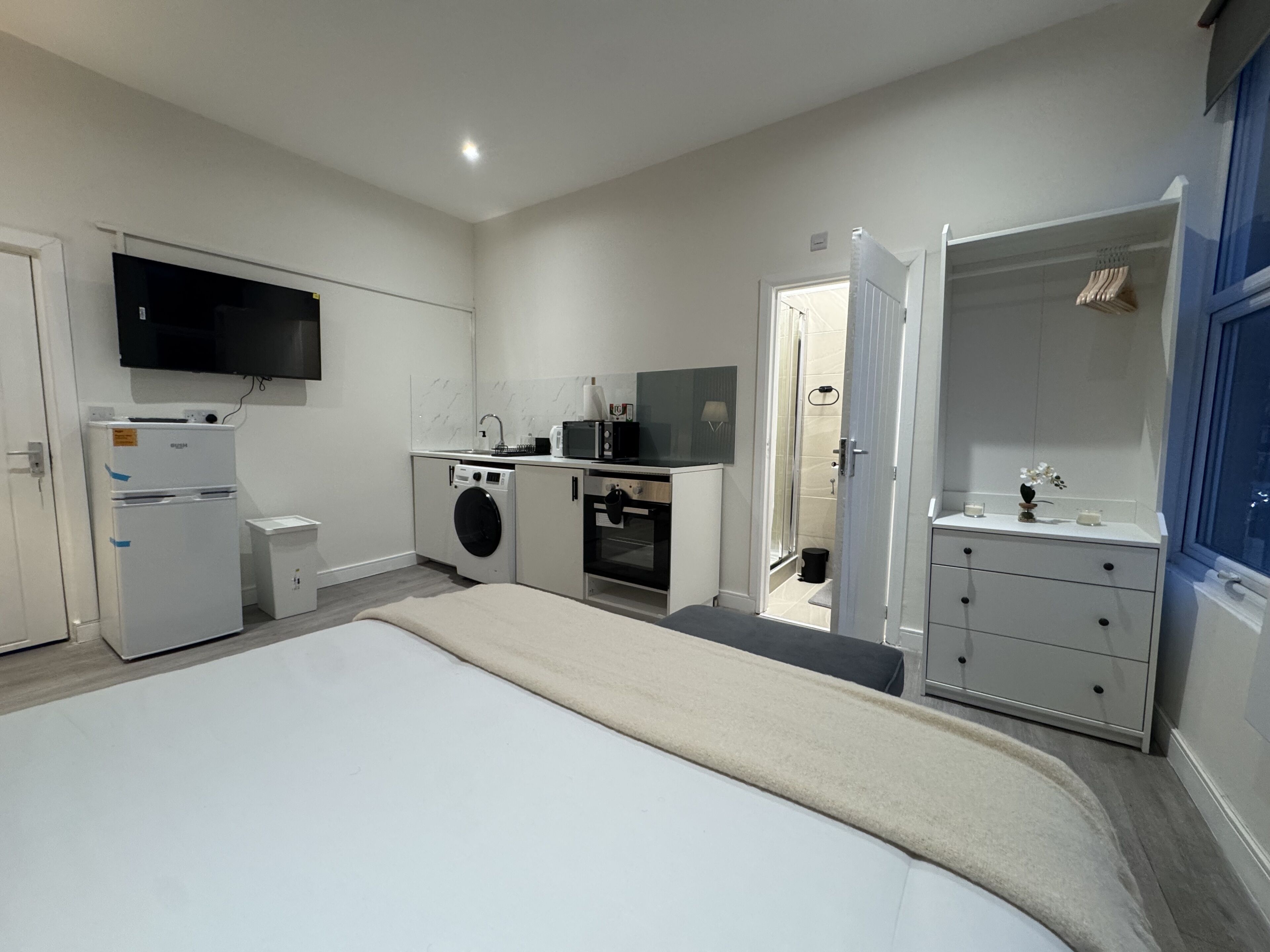 A modern bedroom with a bed, a TV, a washing machine, and a kitchenette.