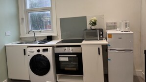 A compact kitchen with a washing machine, microwave, oven, and a small refrigerator. - Hammersmith Haven (London)