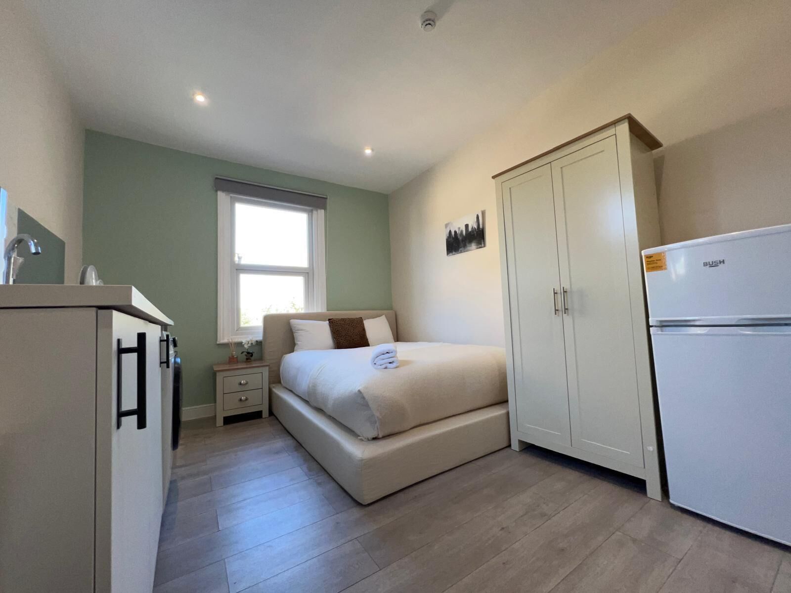 A bedroom with a bed, a nightstand, a wardrobe, and a refrigerator.