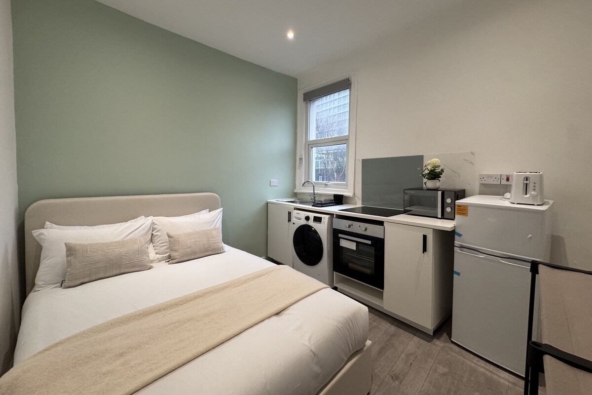 A compact room with a bed, washing machine, microwave, and a small refrigerator.