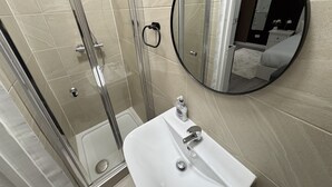 A bathroom with a glass shower enclosure, a white sink, and a round mirror. - Hammersmith Haven (London)