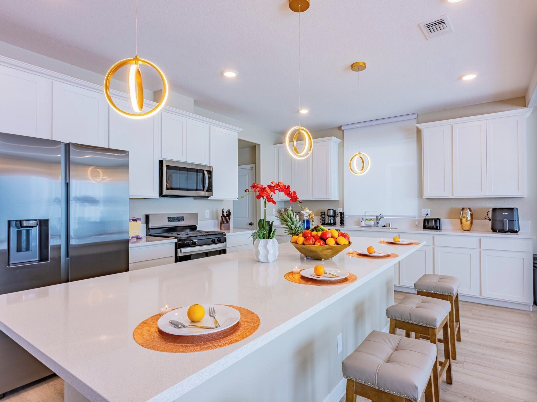 A modern kitchen with white cabinetry, stainless steel appliances, and a central island with a fruit bowl and seating.