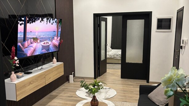 Moderni olohuone, jossa on televisio, sohvapöytä ja huonekasvi.