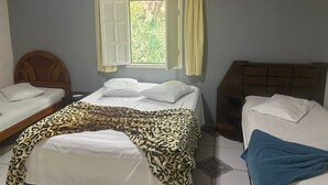 Een kamer met twee bedden, een raam met gordijnen en uitzicht op groen.