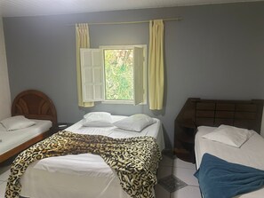 A room with two beds, a window with curtains, and a view of greenery outside. - pousada do pc (Bom Jesus do Itabapoana)