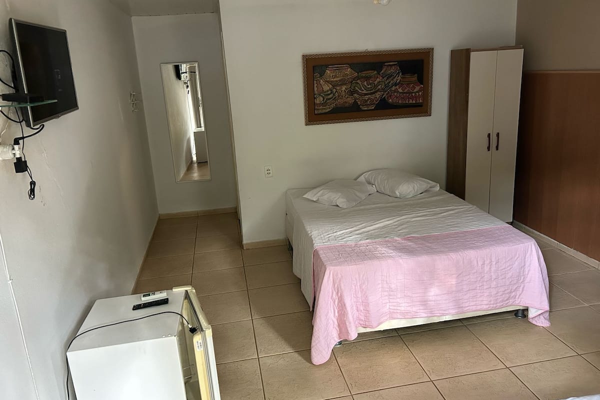 A bedroom with a bed, a wardrobe, a television mounted on the wall, and a ceiling fan.