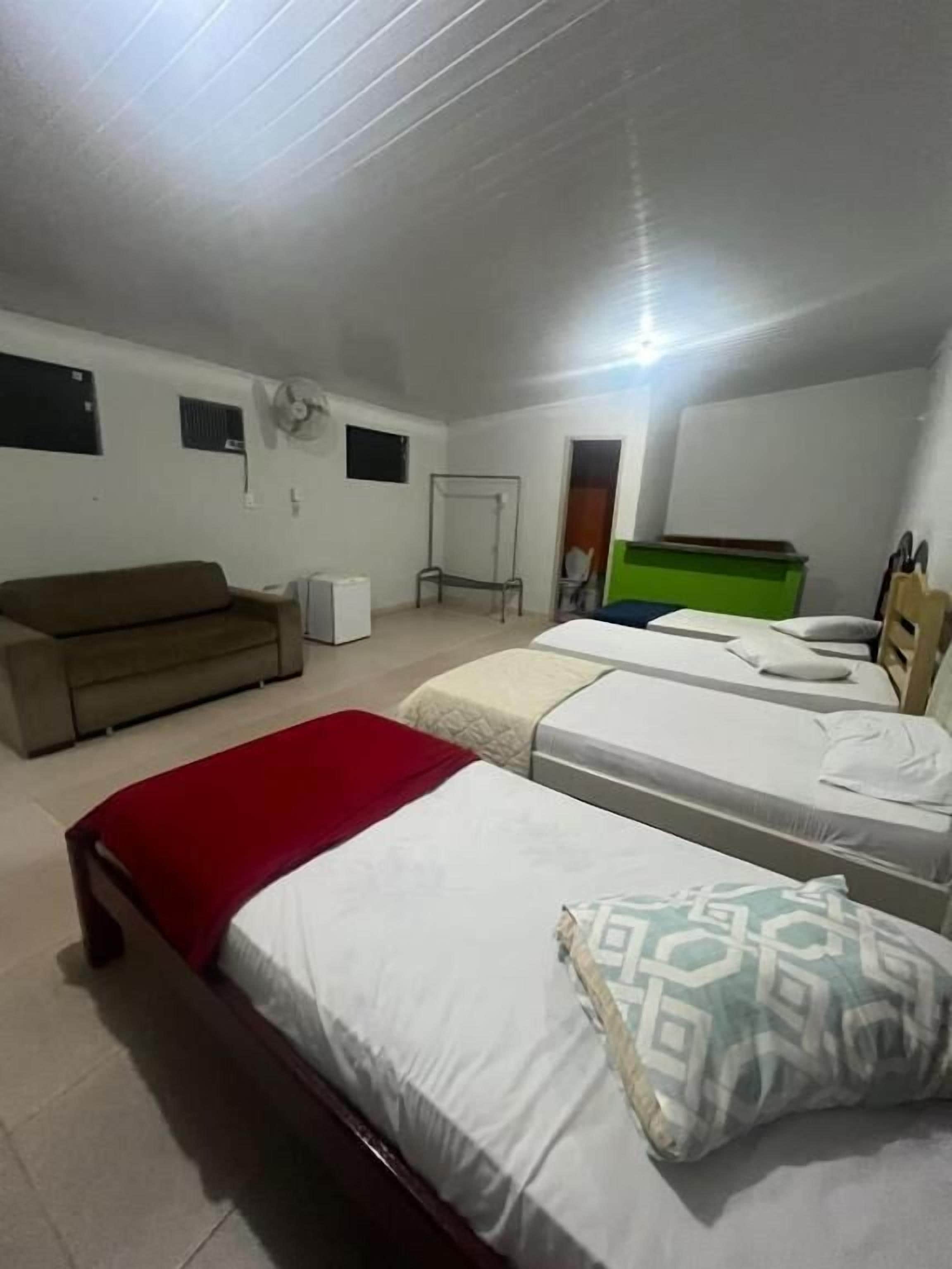 Een kamer met twee bedden, een slaapbank, een ventilator en een groene opbergunit.