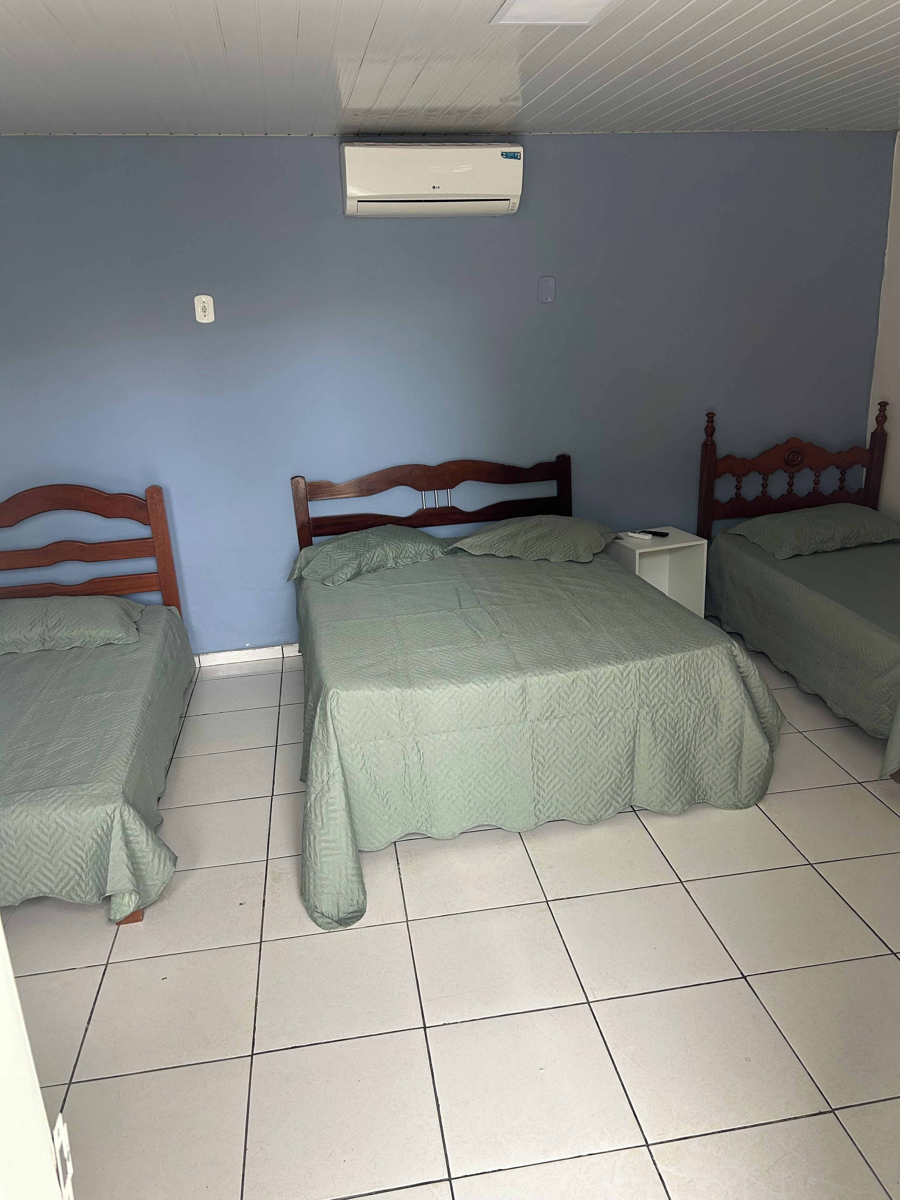 Een kamer met twee bedden, een houten hoofdbord, een witte nachtkastje en een aan het plafond bevestigde airconditioner.