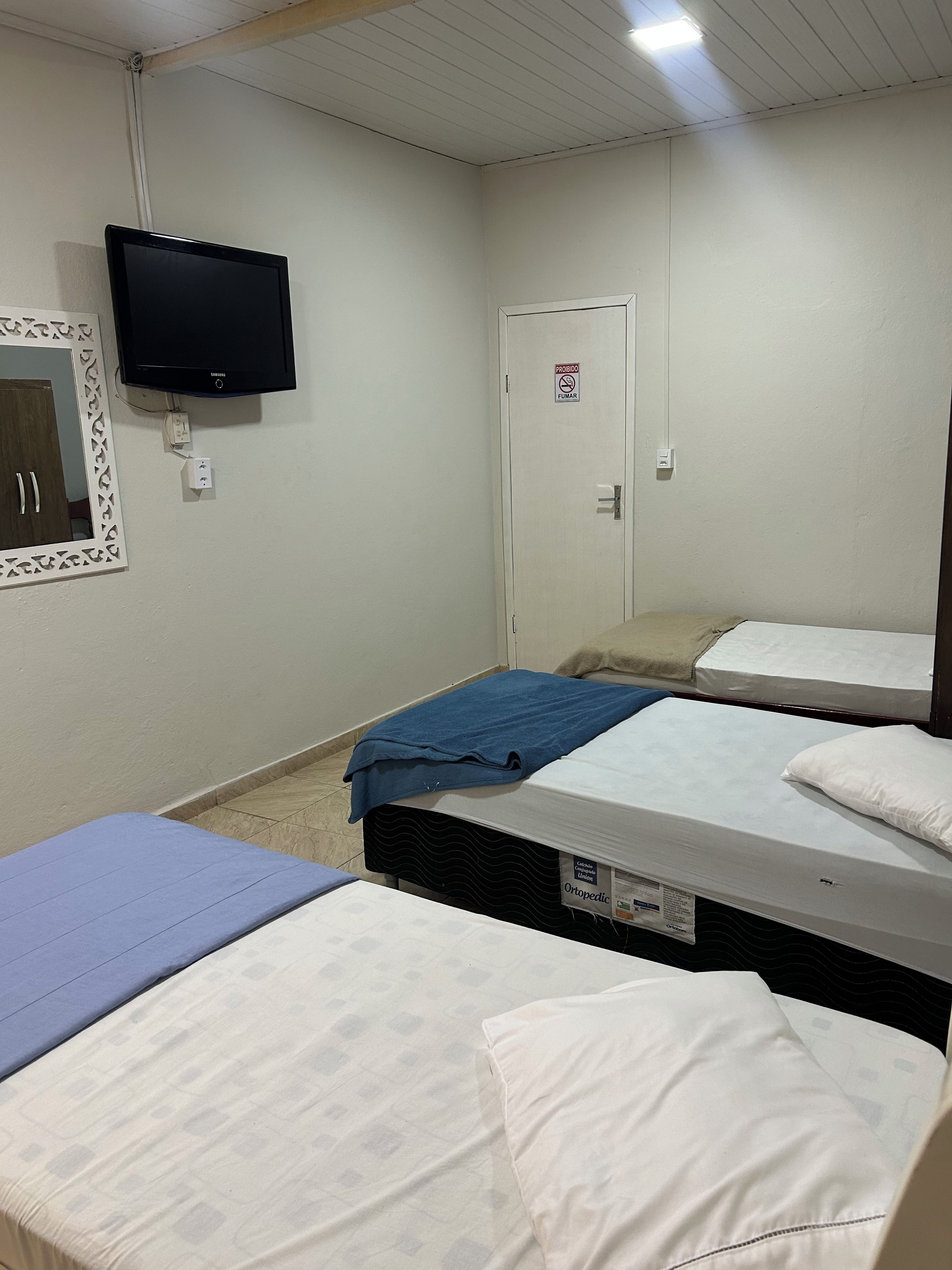 Una habitación con dos camas, televisión y una puerta con el letrero 'no fumar'.