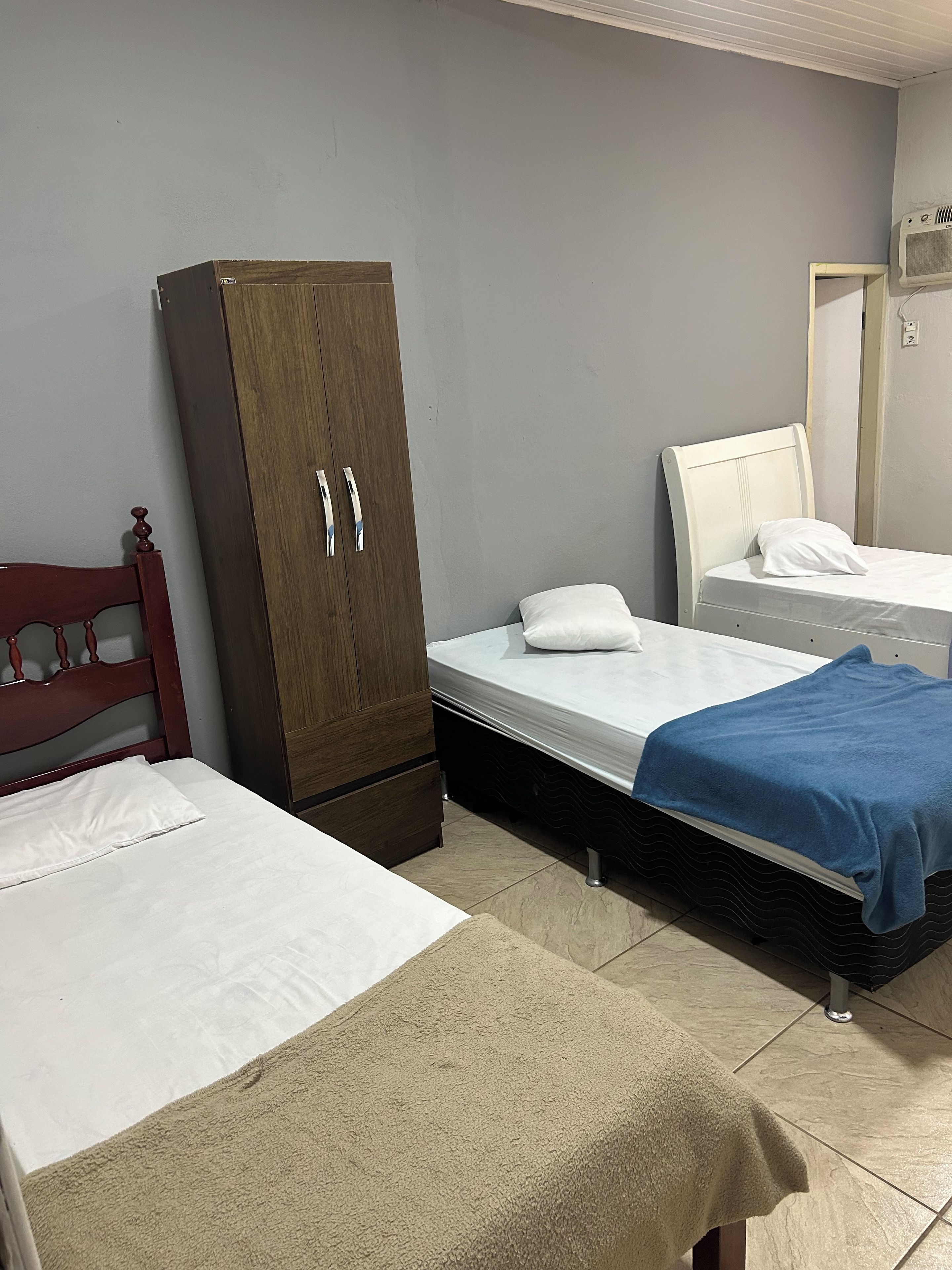Una habitación con dos camas, un armario y aire acondicionado instalado en la pared.
