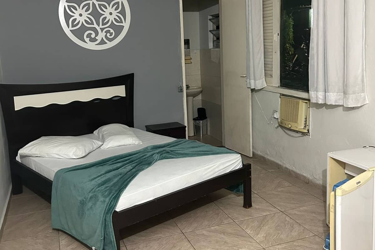 A bedroom with a bed, a ceiling fan, a wall decoration, a window with curtains, and a small bedside table.