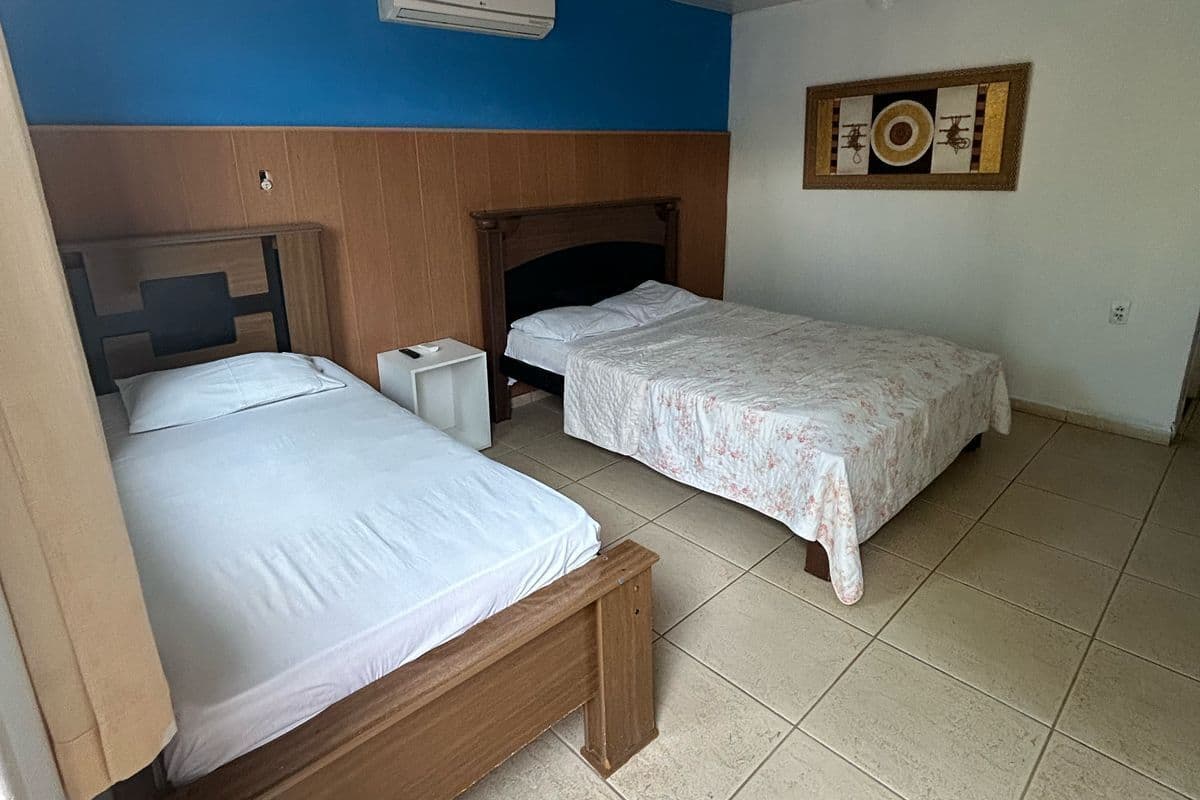 A bedroom with two beds, an air conditioner, a ceiling fan, and a decorative wall piece.