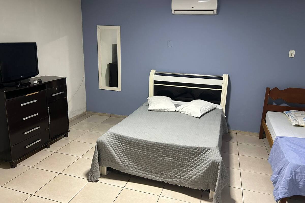 A bedroom with a bed, a dresser, a television, a mirror, and an air conditioning unit.
