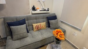 Un canapé gris avec un coussin orné du mot «Relax», un vase rempli de fleurs oranges et un tableau représentant un palmier accroché au mur.