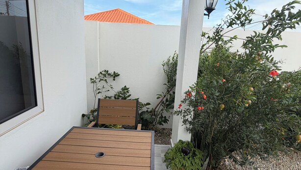 Une terrasse avec une table et des chaises, entourée de plantes et offrant une vue sur un bâtiment dont le toit est rouge.