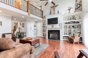 A spacious living room with a fireplace, wooden flooring, and a high ceiling with a fan. - Beary Relaxing, Smoky Mt Cabin that sleeps 10! (Bryson City)