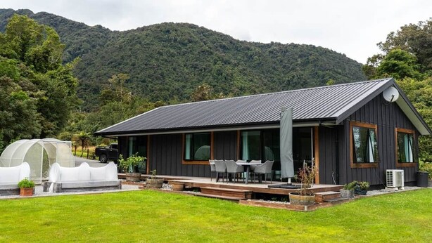 A modern house with a large deck, a greenhouse, and a mountain backdrop.