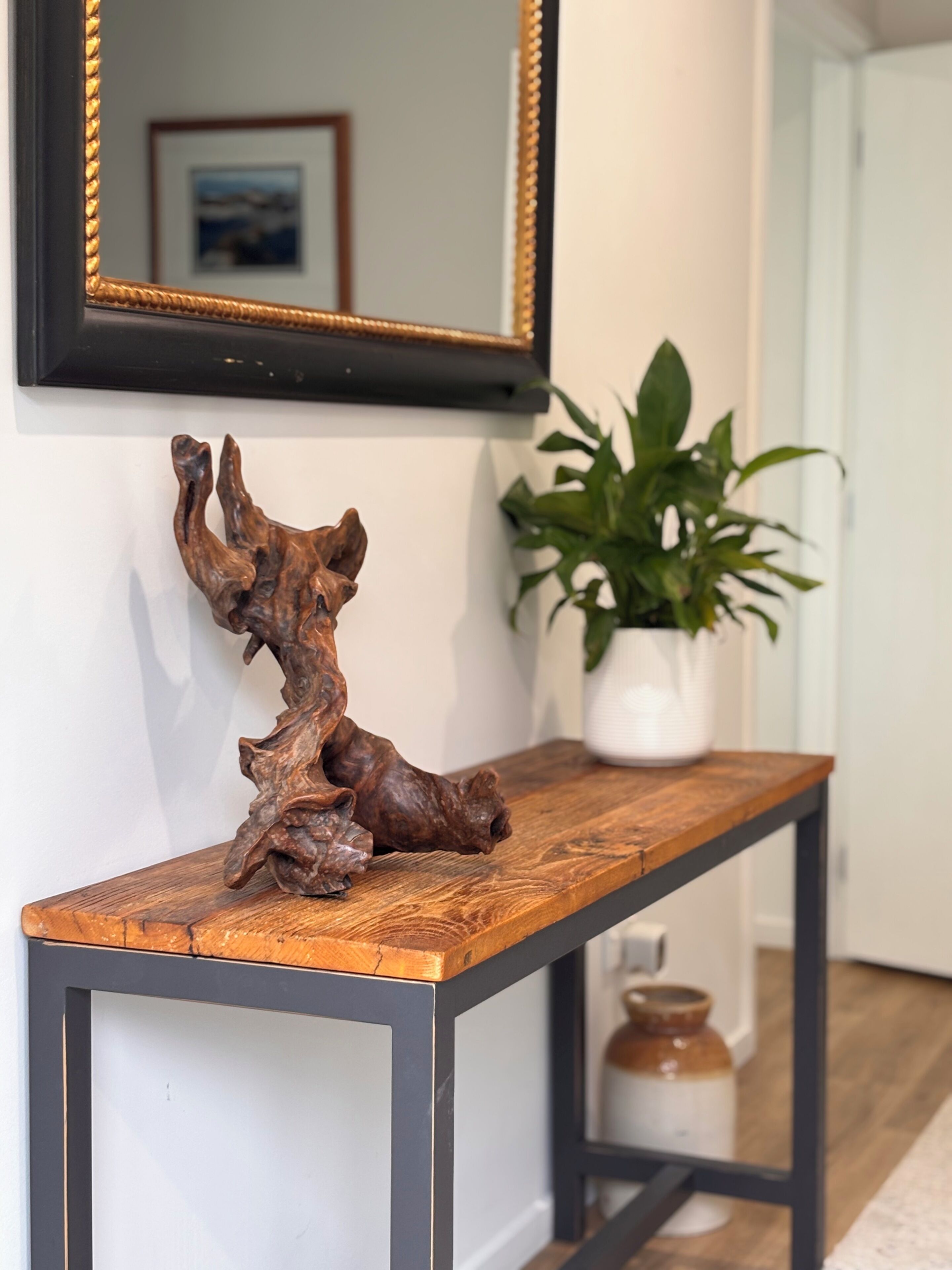 Une console en bois ornée d’une sculpture, d’un miroir et d’une plante en pot.