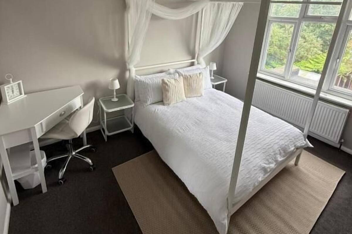 A bedroom with a four-poster bed, a desk, and a chair.