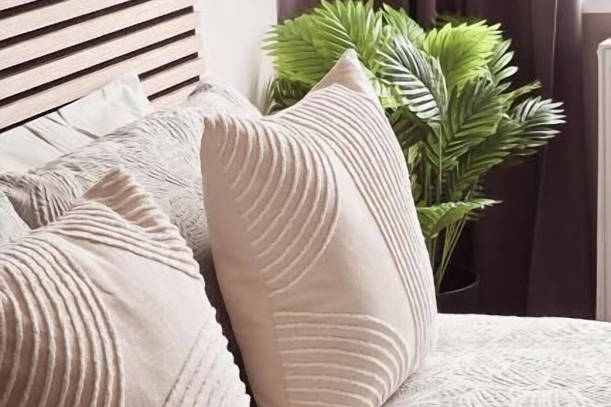 A bed with a textured white bedspread, a wooden slatted headboard, and two beige pillows with a ribbed design.