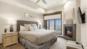 Een slaapkamer met een groot bed, een open haard, een aan de muur bevestigde televisie en een raam met uitzicht.