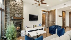 Een woonkamer met een open haard, een flatscreen televisie, een plafondventilator en een blauwe bank.