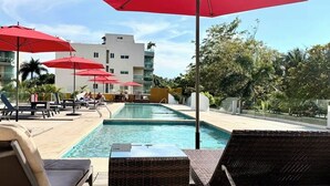 Ein Poolbereich mit roten Sonnenschirmen, Liegestühlen und einem Gebäude im Hintergrund.