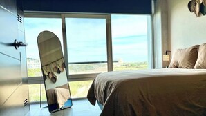 Ein Schlafzimmer mit einem Bett, einem großen Fenster und einem Spiegel.